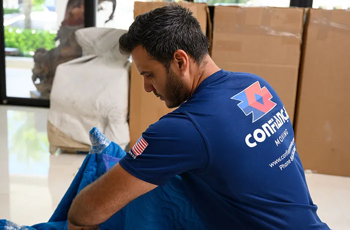 Confiança mover in company t-shirt wrapping furniture in a blue blanket