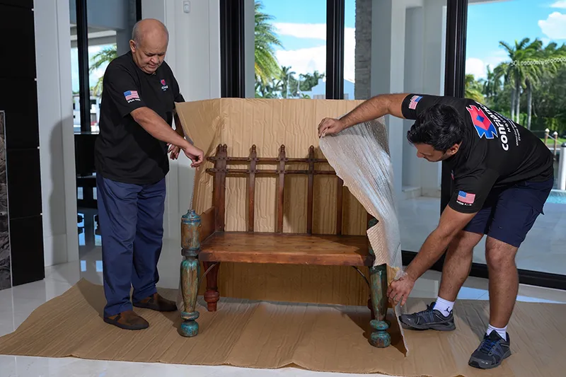 Two Confiança movers wrapping a wooden bench in cardboard