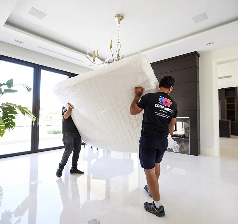 Confiança movers carrying a wrapped mattress through a bright home