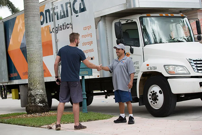 Confiança mover shaking hands with a client beside the company truck