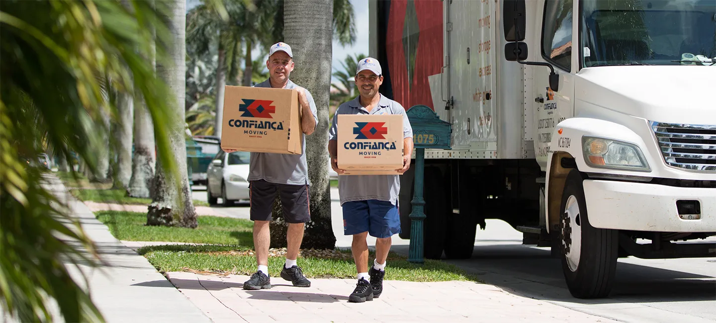 Two Confiança movers carrying branded boxes next to the company truck